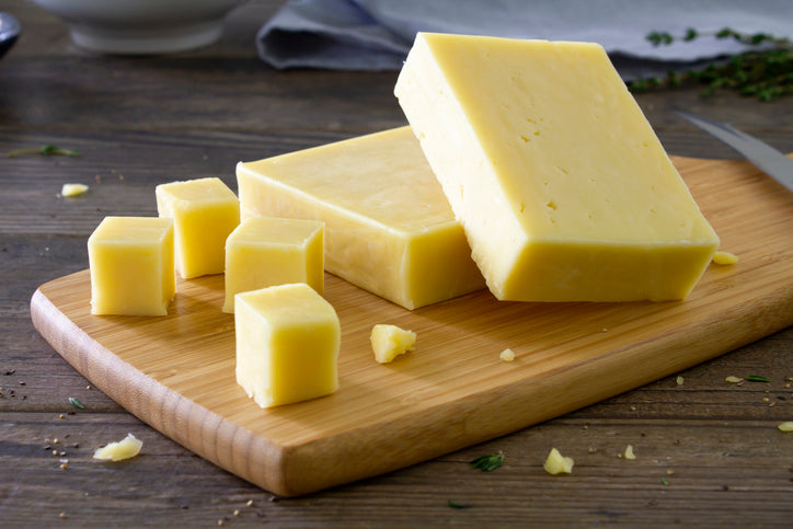 Block of raw milk cheese on cutting board, aged and cut from A2A2 milk