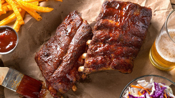 A photo of cooked beef back ribs with a visible marbled pattern, served with fries, coleslaw, and a drink.