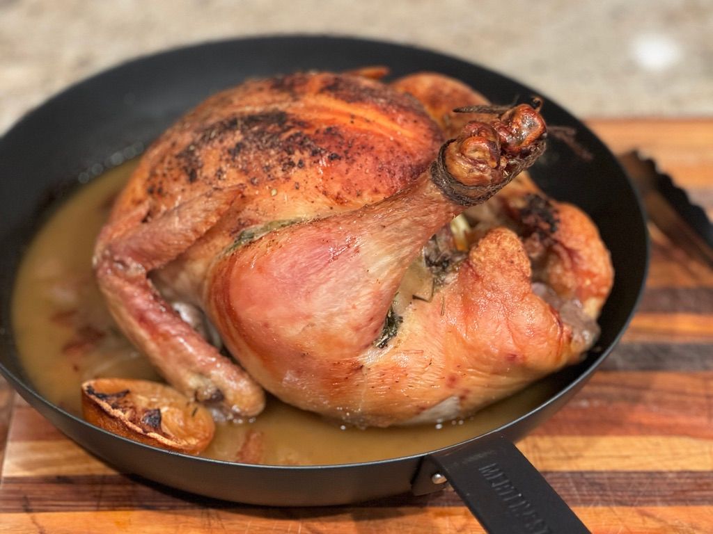 Whole roast chicken in cast iron pan with rendered juices, pasture-raised