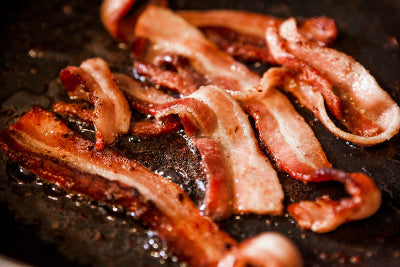 Chewy bacon frying in skillet, close-up showing texture and fat rendering