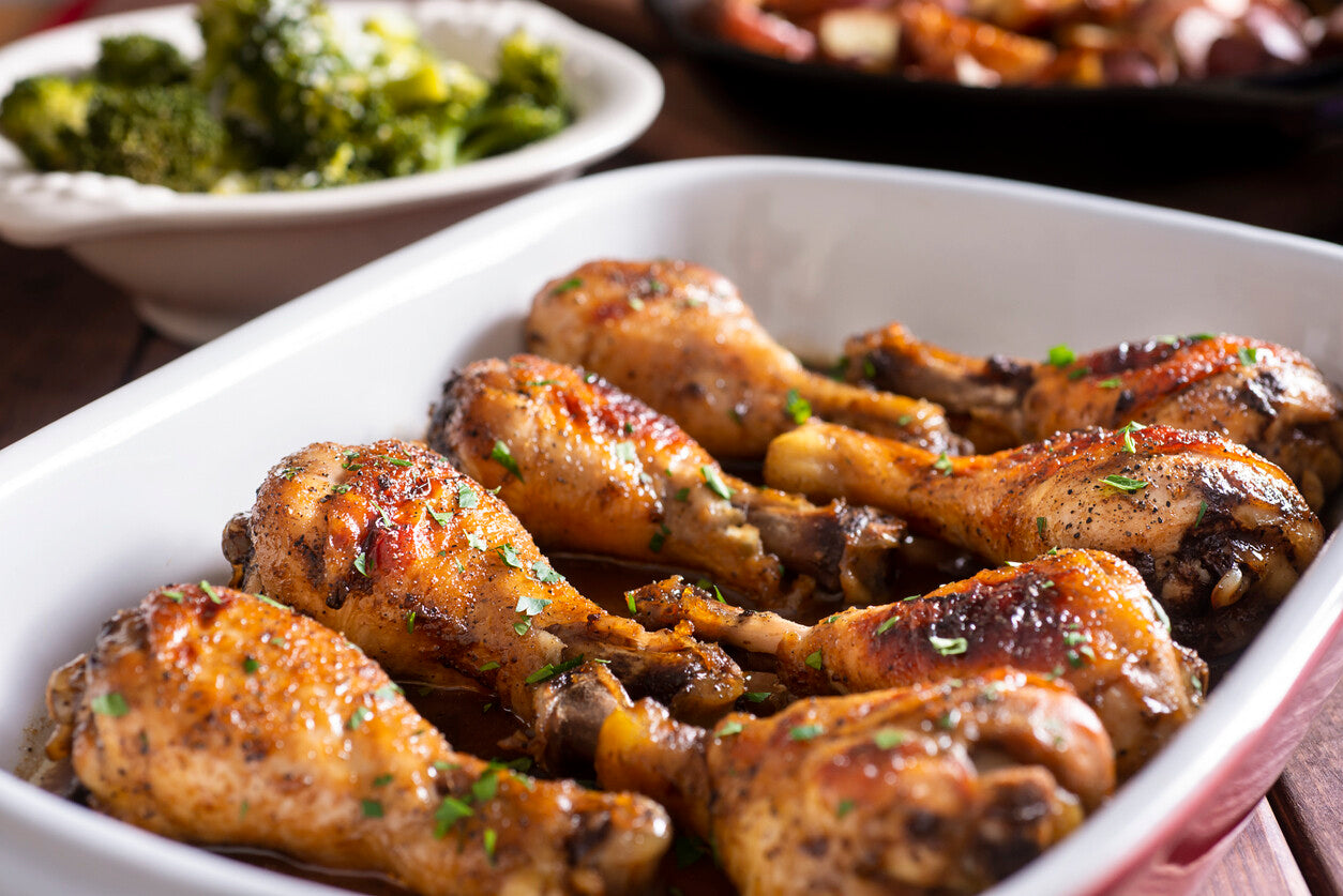 Cooked pasture-raised chicken drumsticks in white Pyrex dish, skin-on and bone-in