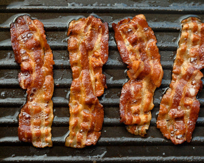 Strips of crispy bacon cooking on griddle, evenly browned and curled