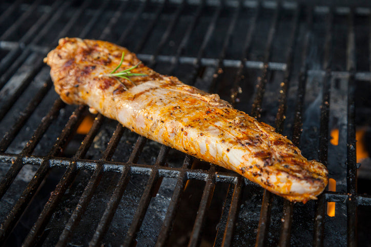 Pork tenderloin grilling over open flame, browning evenly