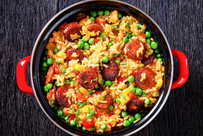 Top-down view of jambalaya with sliced kielbasa in red Dutch oven