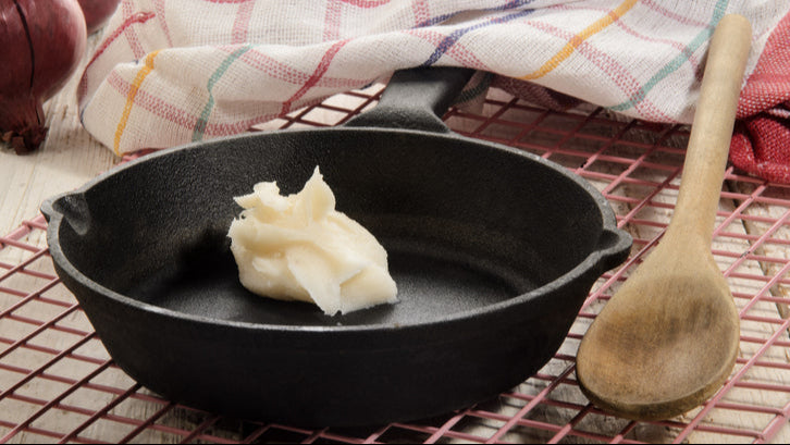 Scoop of pork lard melting in cast iron frying pan
