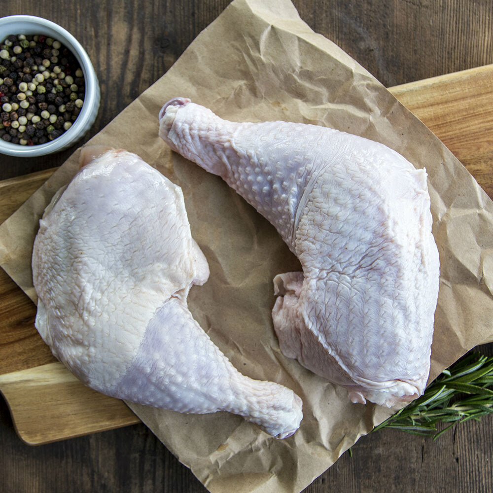 Raw pasture-raised chicken leg quarters on butcher paper, skin-on and bone-in from Tyner Pond Farm