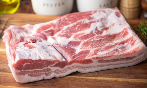 Raw pork belly slab on cutting board, trimmed and ready for cooking or curing