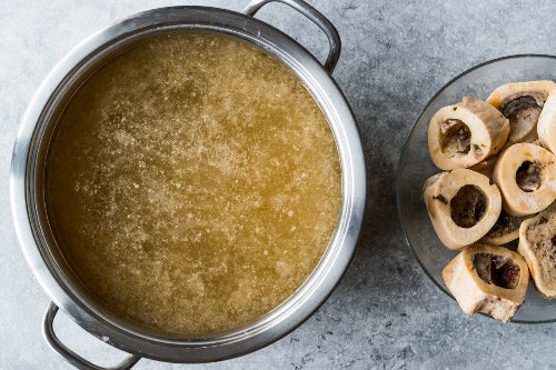 Top-down view of finished beef bone broth with soup bones and herbs