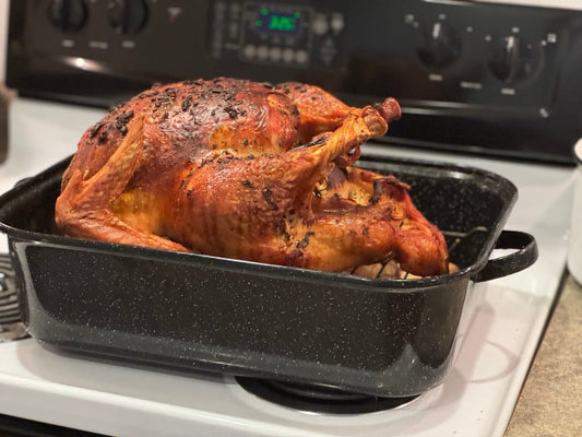 A golden-brown roasted pasture-raised turkey from Tyner Pond Farm, sitting in a black roasting pan on a stovetop, prepared with herb butter and aromatic stuffing