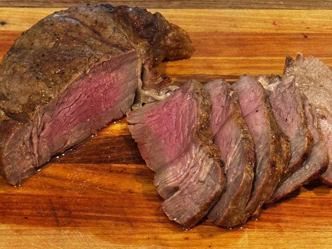 Sliced medium-rare grass-fed sirloin steak cooked in an air fryer, displayed on a wooden cutting board.