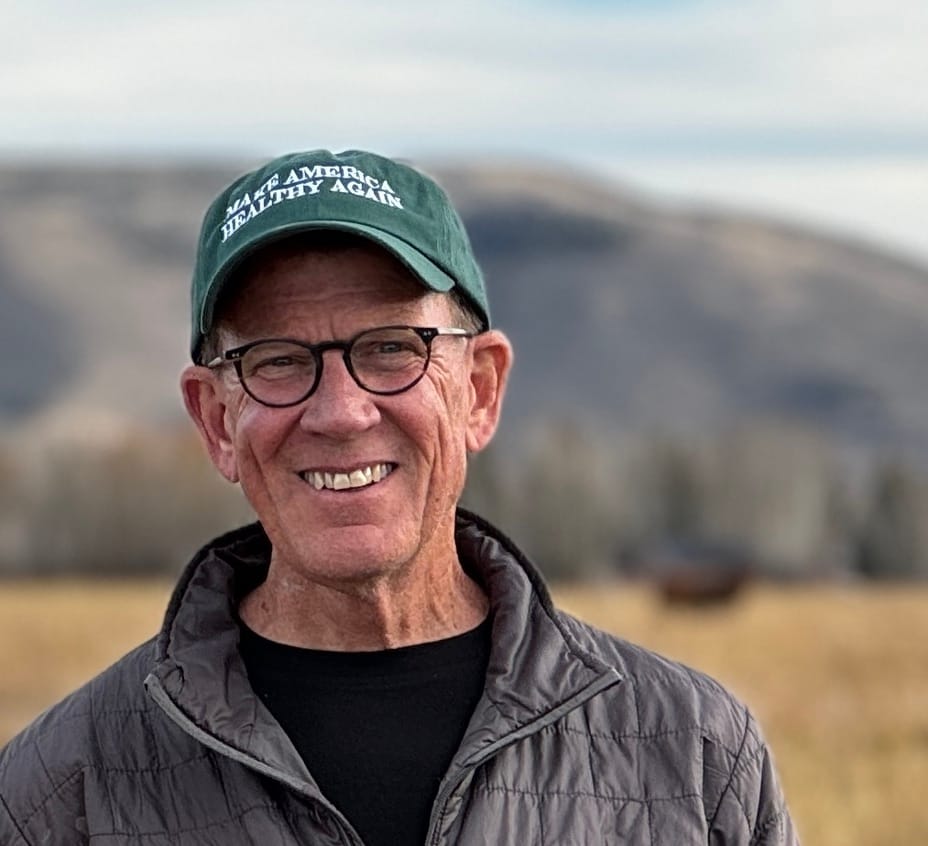 Chris Baggott, founder of Tyner Pond Farm, standing outdoors with a pasture and grazing animals in the background, promoting sustainable and regenerative farming practices.