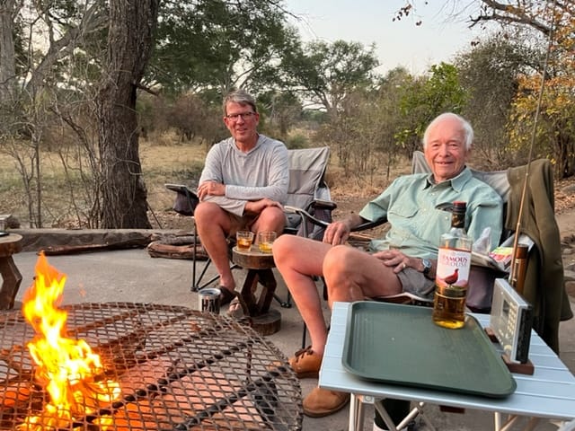 Chris Baggott and Allan Savory sitting outdoors near a fire, engaged in conversation about holistic management and regenerative agriculture in Africa.