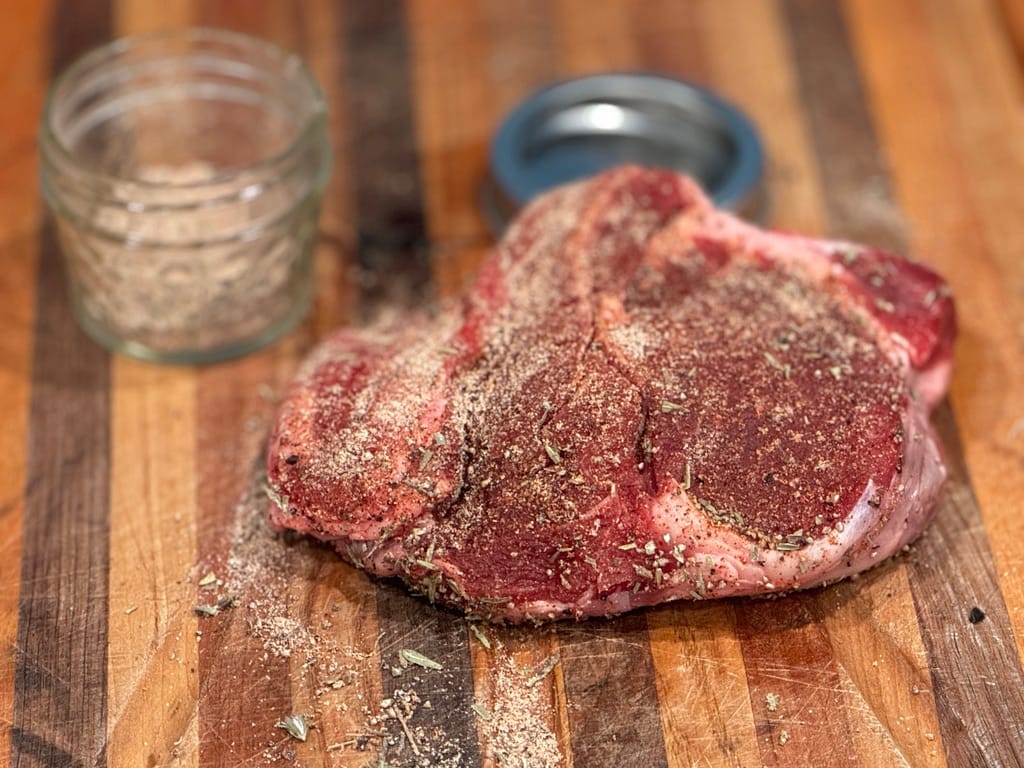 Grass-fed steak with a homemade seasoning rub on a wooden cutting board, ready for grilling.