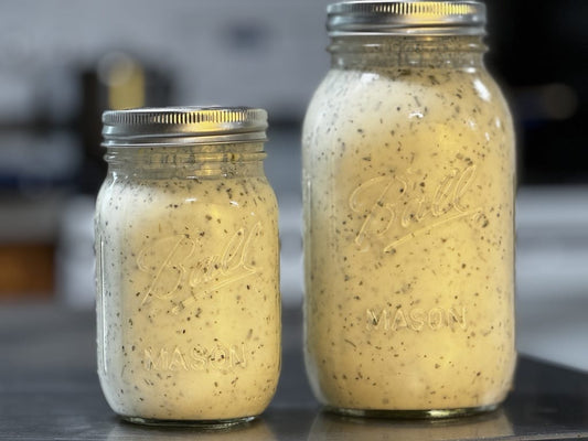 Two mason jars filled with homemade yogurt ranch dressing. The dressing has a creamy texture with visible specks of herbs throughout.