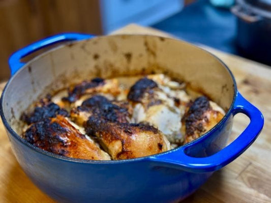 A Dutch oven with golden-brown roasted chicken pieces on top of cooked vegetables, fresh out of the oven.