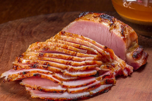 Sliced honey-glazed ham on a wooden cutting board, showcasing a golden caramelized crust with tender, juicy interior slices.