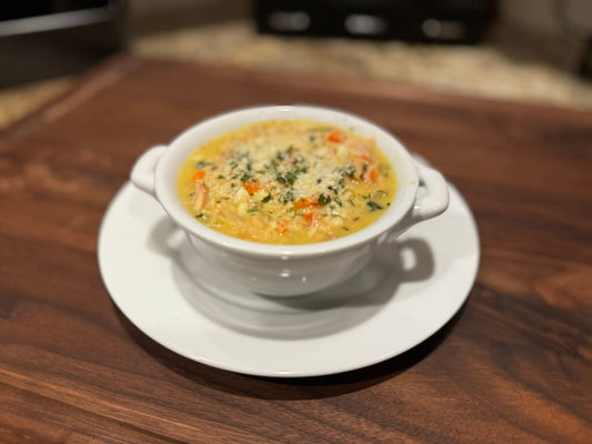 A warm bowl of chicken orzo soup with carrots and fresh herbs, made with pasture-raised chicken and served in a white bowl on a wooden surface.