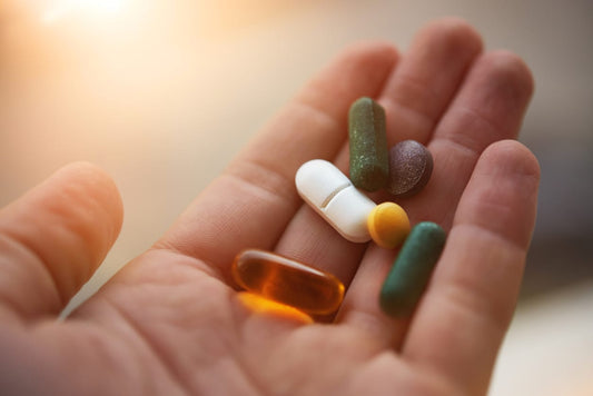 Hand holding a variety of dietary supplements, representing the debate over supplement use and the need for nutrient-dense food.
