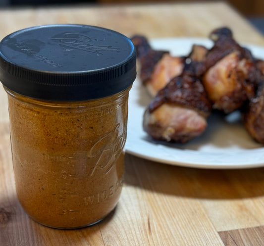 A glass mason jar filled with smoky chipotle ranch dressing next to a plate of smoked chicken legs on a wooden surface.