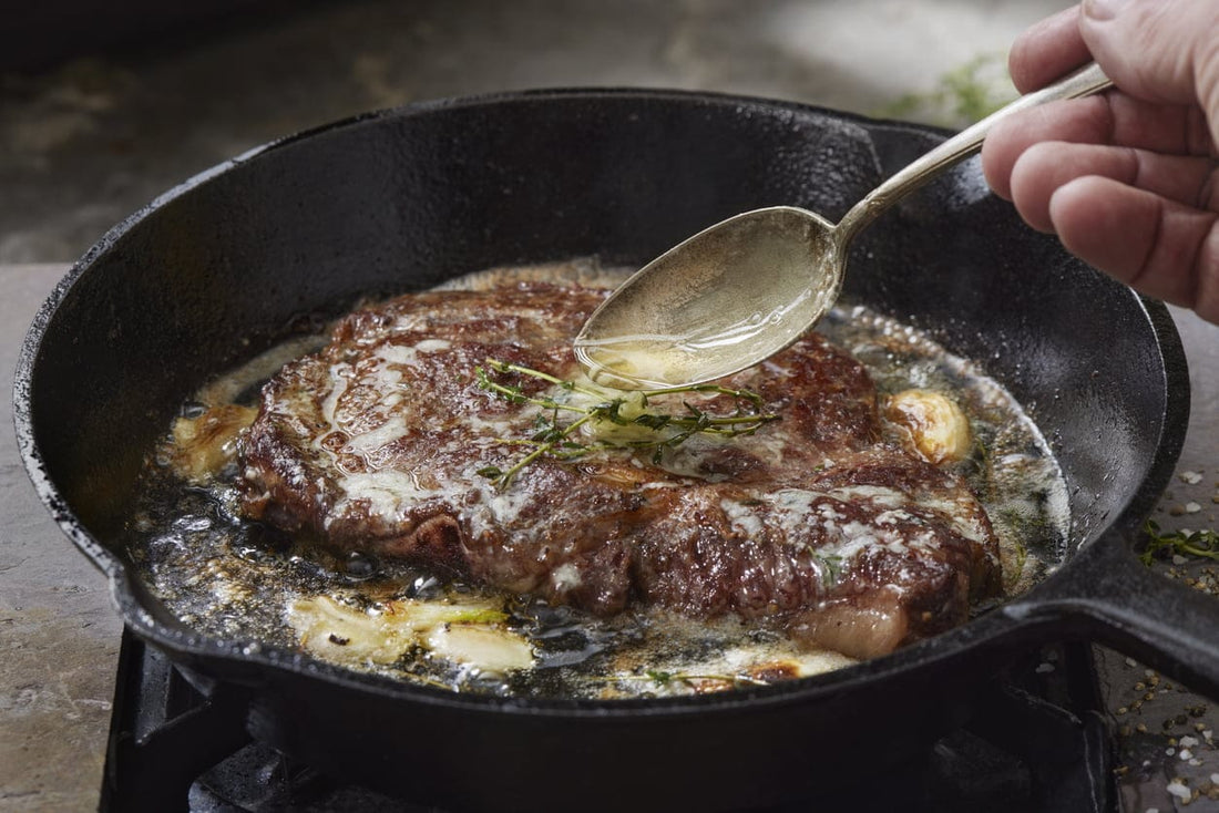 A grass-fed steak being basted with melted butter and herbs in a cast iron skillet, highlighting the benefits of even heat distribution and superior searing