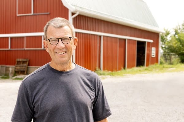 Chris Baggott, co-owner of Tyner Pond Farm, standing in front of a red barn, discussing the role of food in addressing nutritional health, particularly focusing on grass-fed beef and vitamin B12.