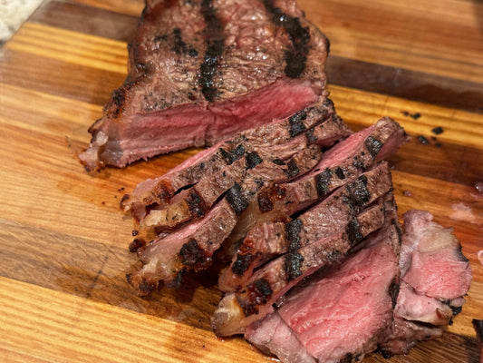 Sliced grilled grass-fed steak showing a tender, juicy interior with seared grill marks on a wooden cutting board.