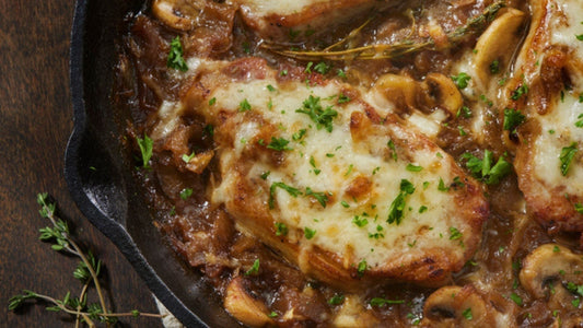 French onion boneless pork chops topped with caramelized onions, mushrooms, and melted Swiss cheese in a skillet