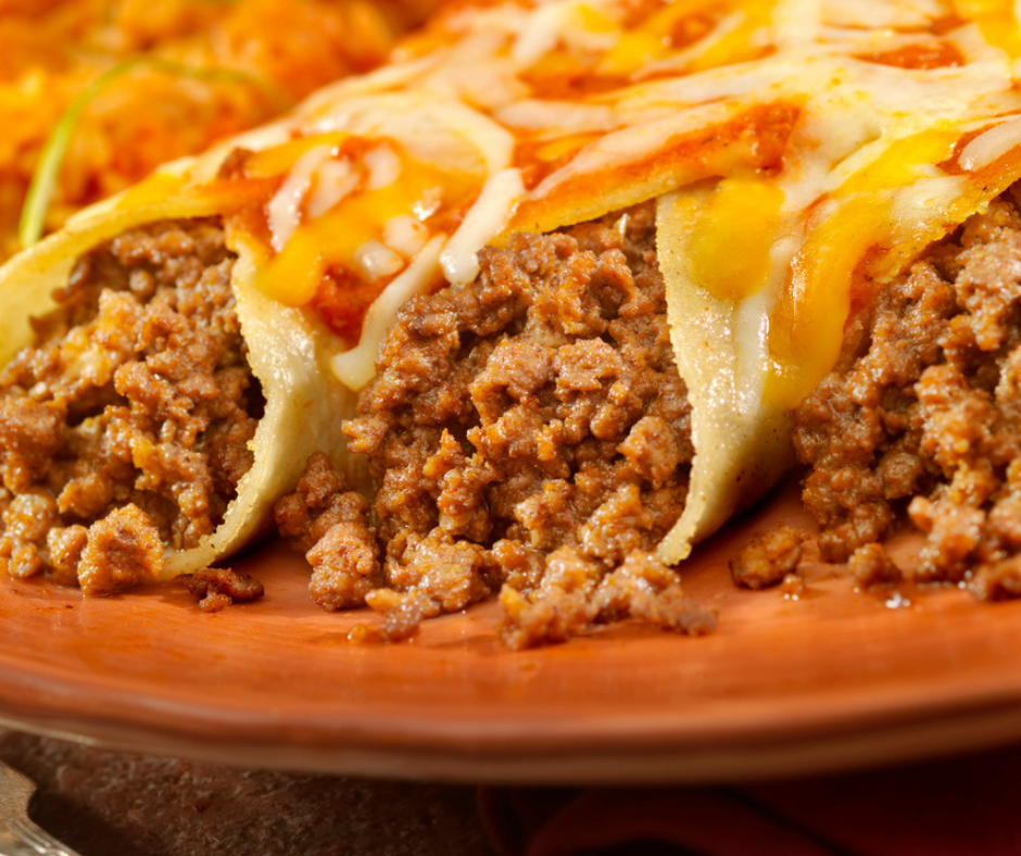Close-up of authentic Mexican beef enchiladas made with grassfed beef, topped with melted cheese and sour cream on a rustic plate.
