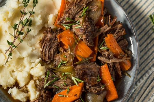 A plate of tender slow-cooked chuck roast with carrots and onions, served alongside creamy mashed potatoes, garnished with fresh rosemary.