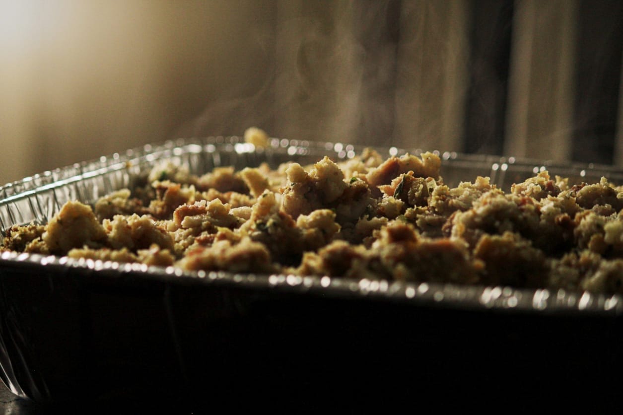Steaming tray of homemade Thanksgiving stuffing with a golden, rustic texture, served in a foil dish.