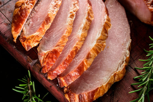 Sliced, keto-friendly baked ham with a golden brown crust on a wooden cutting board, garnished with fresh rosemary.