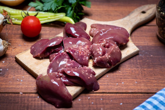 Fresh pasture-raised chicken livers on a wooden cutting board, garnished with coarse salt, surrounded by fresh vegetables.