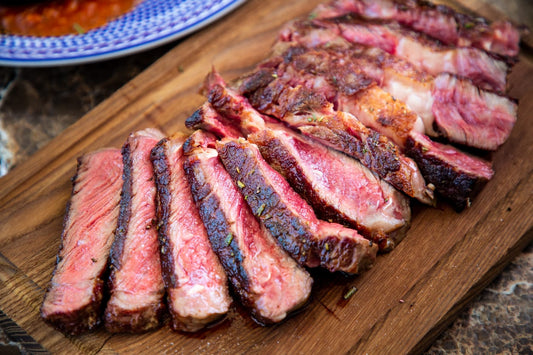 Sliced, medium-rare grass-fed cull cow steak on a wooden cutting board, showing a deep sear and pink interior. The steak has a rich crust and is cut against the grain for maximum tenderness.