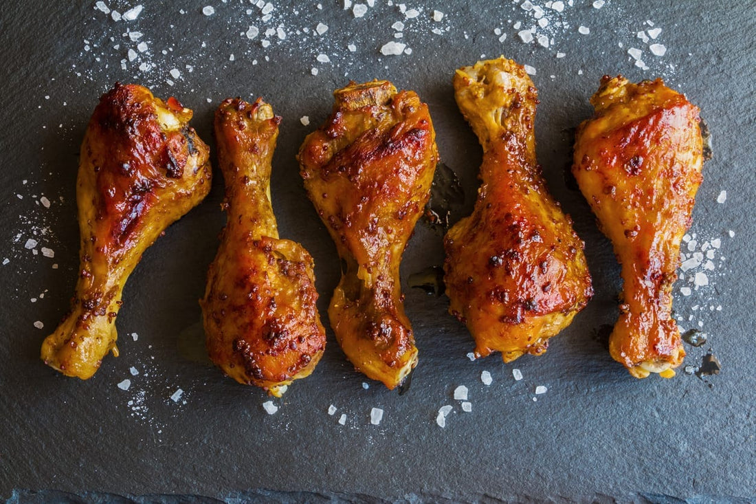 Five roasted pasture-raised chicken drumsticks with crispy skin on a slate surface, garnished with sea salt flakes