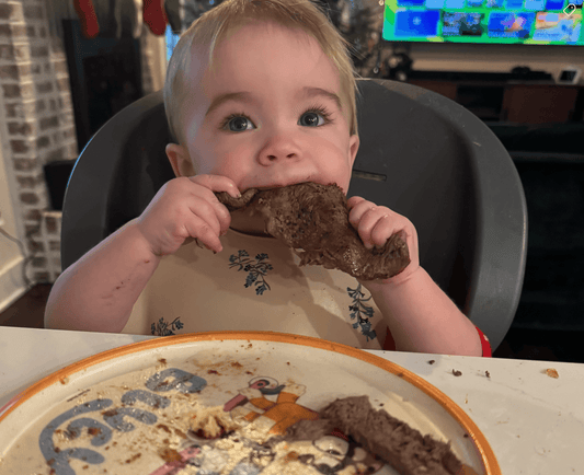 A baby seated in a highchair exploring soft, whole foods with their hands, demonstrating the baby-led weaning approach.