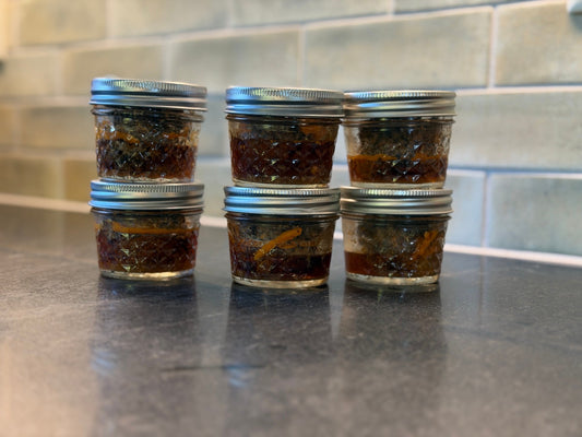Six small glass jars of Chris’s homemade chorizo stacked in pairs on a kitchen counter.