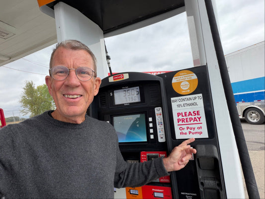 Chris Baggott at a gas pump pointing at the may contain up to 10 percent ethanol sticker