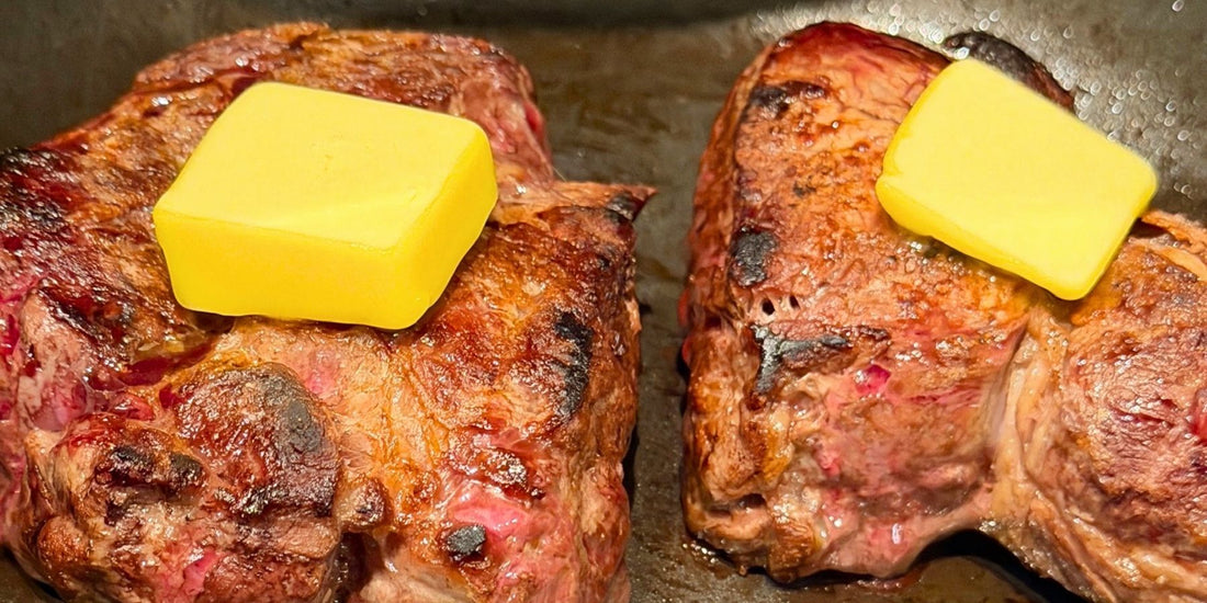 Grass-fed beef steaks cooked in a cast iron pan with butter melting on top