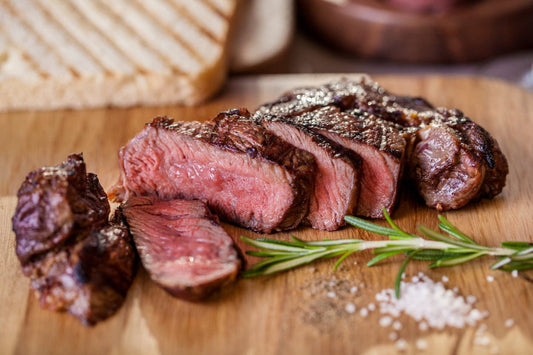 High-quality grilled beef steak slices on a wooden board with rosemary, salt, and pepper, highlighting the benefits of properly frozen meat.