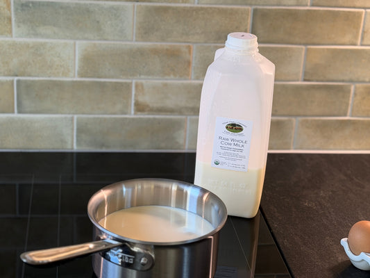 Half-gallon jug of Kemp Family Organic raw whole cow milk beside a saucepan of milk