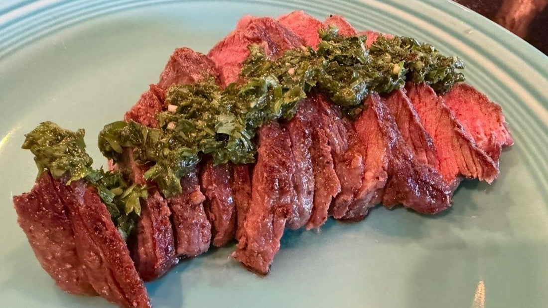 Sliced grassfed Denver steak topped with fresh parsley chimichurri on a blue plate.