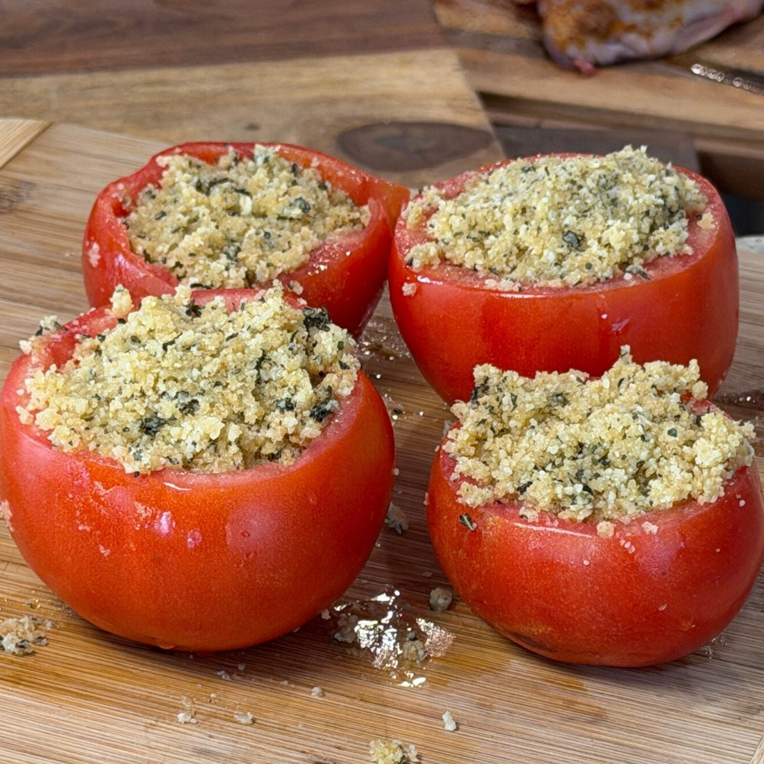 Four fresh, hollowed-out summer tomatoes stuffed with a crispy low-carb Parmesan and ground pork rind panko topping, resting on a wooden cutting board in the Tyner Pond Farm kitchen