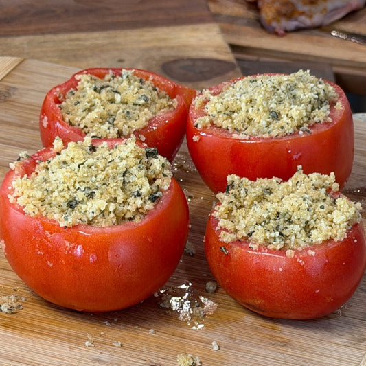 Four fresh, hollowed-out summer tomatoes stuffed with a crispy low-carb Parmesan and ground pork rind panko topping, resting on a wooden cutting board in the Tyner Pond Farm kitchen