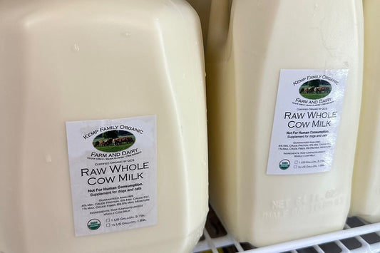 A gallon and a half gallon of raw whole cow milk from Kemp Family Organic Farm and Dairy, labeled USDA Organic, on a refrigerator shelf