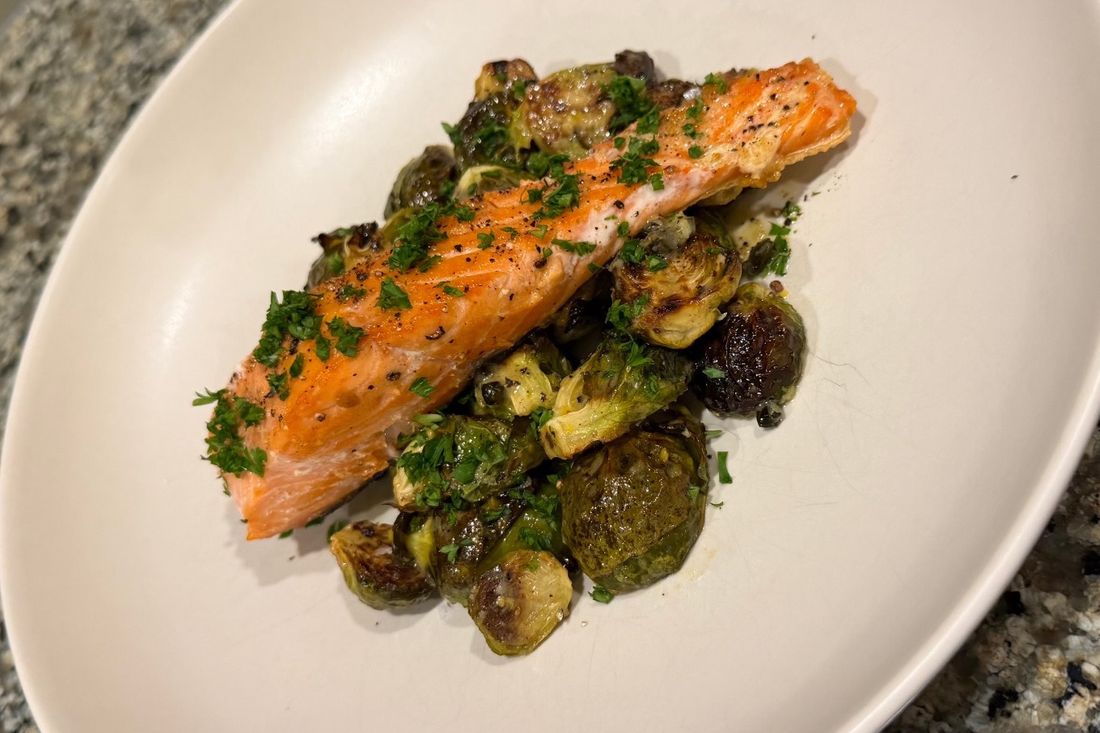 Cooked salmon topped with chopped herbs, served over Brussels sprouts on a white plate.