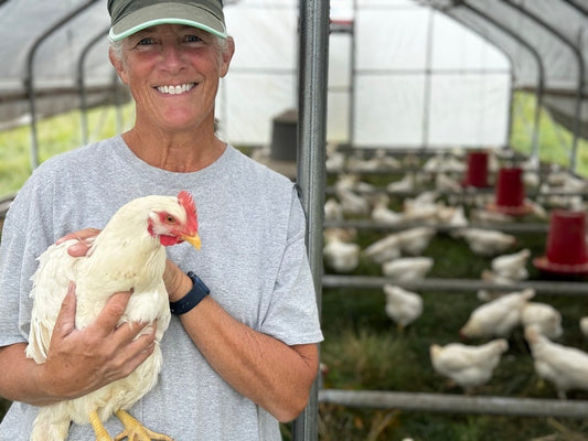 Amy holding a white chicken inside a mobile hoop house, with chickens on grass behind her at Tyner Pond Farm.