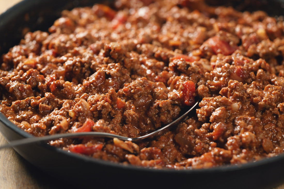 Bolognese sauce in a black pan with a metal spoon.