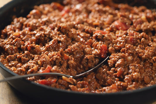 Bolognese sauce in a black pan with a metal spoon.