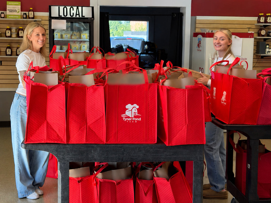 Kristen and Chloe standing behind red Tyner Pond Farm bags packed for delivery.