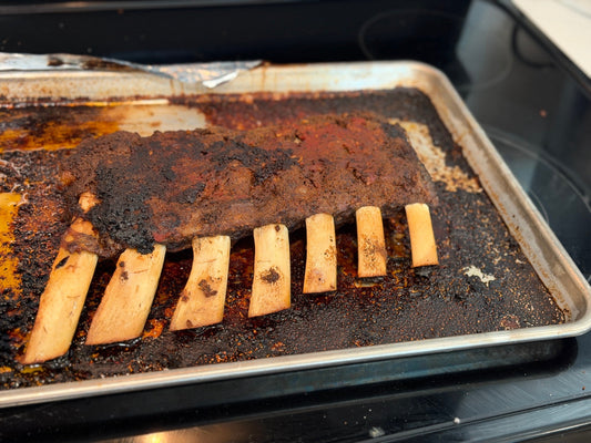 Cooked beef back ribs with exposed rib bones and browned seasoning on a rimmed metal sheet pan.